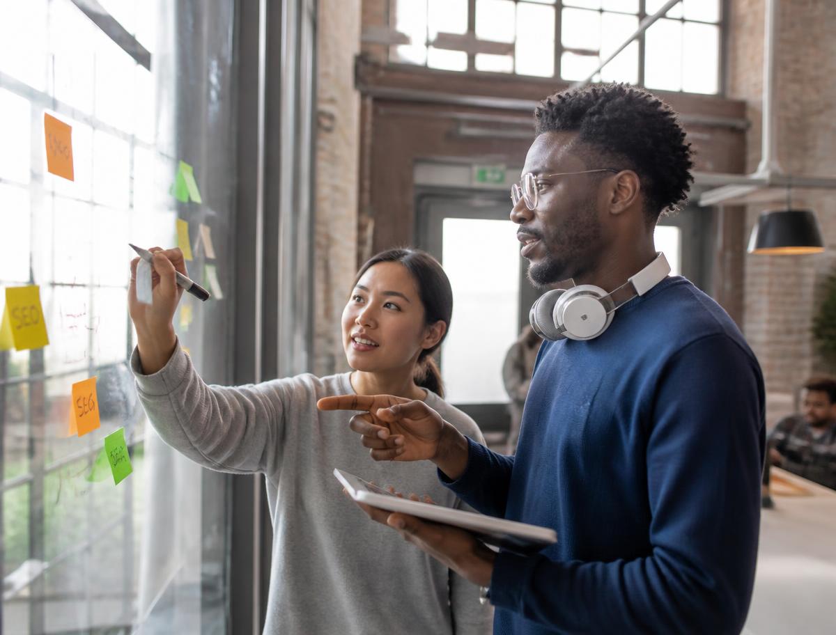 Two founders sketching an idea on a glass wall covered in sticky notes